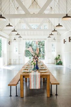 a long wooden table with plates and place settings on it in a large white room