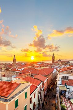 the sun is setting over an old town with red tile roofs and green shutters