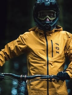 a man wearing a yellow jacket and black helmet riding a bike in the woods with his hands on his hips