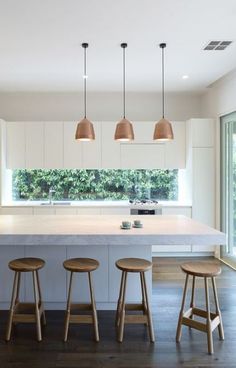 a kitchen with three stools in front of an island counter and four lights hanging from the ceiling