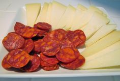 sliced up sausages and cheese in a white dish on a counter top, ready to be eaten