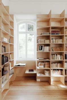 a bookshelf filled with lots of books in front of a window next to a wooden floor