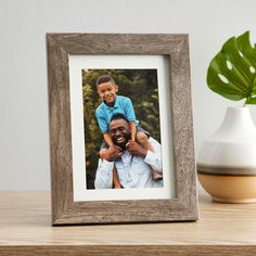 a wooden frame with a photo of a man holding a boy on his shoulders, sitting next to a potted plant