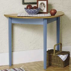 a blue table with an apple bowl on top and a basket under the table next to it