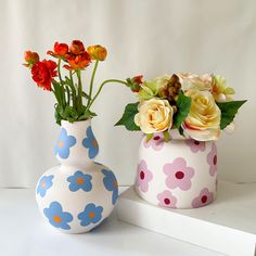 two vases with flowers in them sitting on a white shelf next to each other