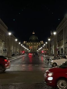 cars driving down the street at night in front of a building with dome on top