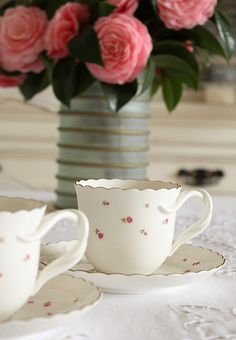 two cups and saucers on a table with pink roses