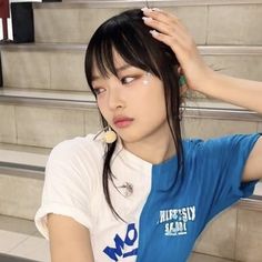 a young woman sitting on the steps with her hand in her hair and wearing a blue shirt