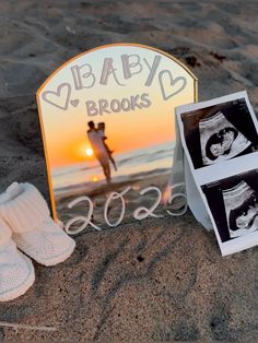 two baby photos are placed on the sand next to an easel and pair of slippers