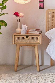 a small table with flowers and books on it in front of a white wall next to a bed