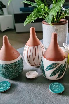 three ceramic vases sitting on top of a table next to a potted plant