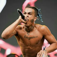 a shirtless man with dreadlocks on his head holding a microphone to his mouth