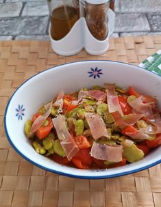 a white bowl filled with lots of food on top of a wooden table next to two bottles