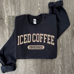 a black sweatshirt with the word iced coffee on it sitting on a wooden floor next to a pair of scissors