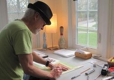 an older man sitting at a desk in front of a window with tools on it