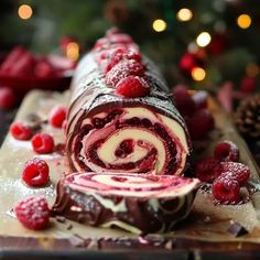 a chocolate roll with raspberries and cream filling on a cutting board next to a christmas tree