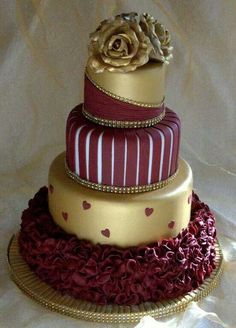 a three tiered cake is adorned with red and gold ribbons, roses, and hearts