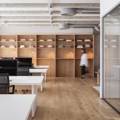 an office with wooden shelves and desks in the center, while a person walks by