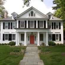 a large white house with black shutters on the front and red door is shown