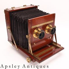 an old fashioned wooden camera sitting on top of a white surface with the words apsley antiques written below it