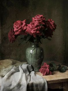 a vase filled with red roses sitting on top of a table next to a blanket