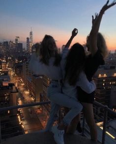 two women standing on top of a building with their arms in the air and one holding her hand up