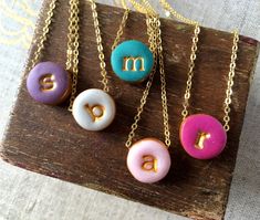 four different colored donuts with the letter m on them hanging from gold chain necklaces