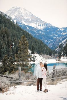 an engaged couple standing in the snow with mountains in the background