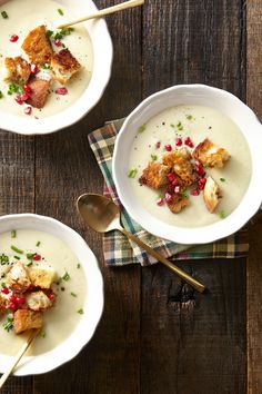 two white bowls filled with soup on top of a wooden table next to spoons