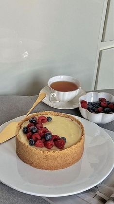 a cheesecake with berries and blueberries on a plate next to a cup of tea