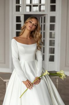 a woman in a white wedding dress holding a yellow flower and posing for the camera