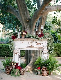 an old fireplace decorated with greenery and candles in front of a large, tree