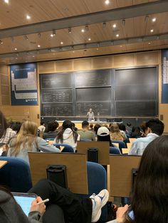 a classroom full of students sitting at desks in front of a chalkboard with writing on it