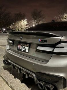 the back end of a silver car parked in a parking lot at night with its lights on