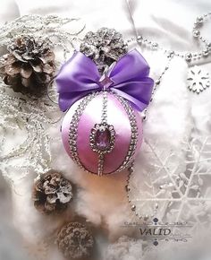 a pink ornament with a purple bow sitting on top of snow covered ground