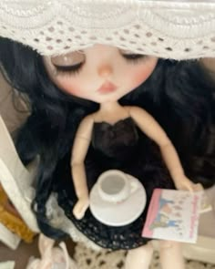 a doll with long black hair is holding a cup and saucer in her hands