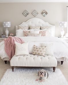 a dog laying on the floor in front of a bed with white sheets and pillows