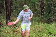 a man holding a pink frisbee in his right hand while walking through tall grass