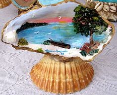 two seashells with paintings on them sitting on a white tablecloth covered table