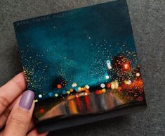 a person holding up a book with fireworks in the sky above it and on the ground