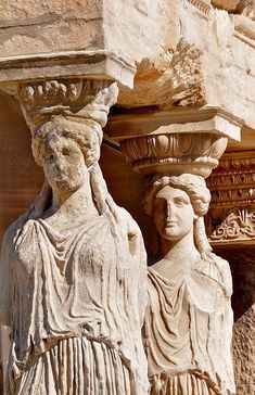 two statues are standing next to each other on the side of a stone building, one is holding a planter