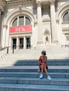 a woman sitting on some steps in front of a large building with columns and windows