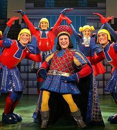 a group of people standing on top of a stage wearing costumes and holding hands in the air