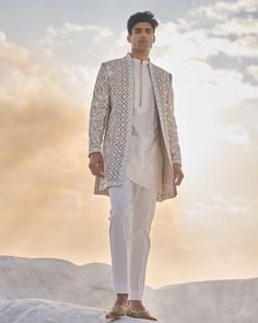 a man standing on top of a snow covered hill wearing a white suit and tie