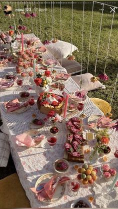 a long table covered in plates and bowls filled with food on top of a lush green field