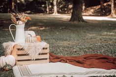 a white pitcher sitting on top of a wooden crate next to a blanket and pumpkins