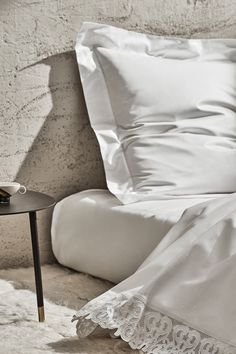 an unmade bed with white sheets and lace on the pillowcase, next to a small side table