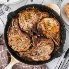 some meat is cooking in a skillet on a table with silverware and utensils