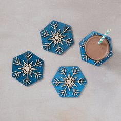 three blue coasters with white snowflakes on them and a drink in the middle