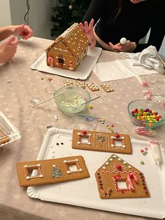 three people sitting at a table with gingerbread houses on it and candy in front of them